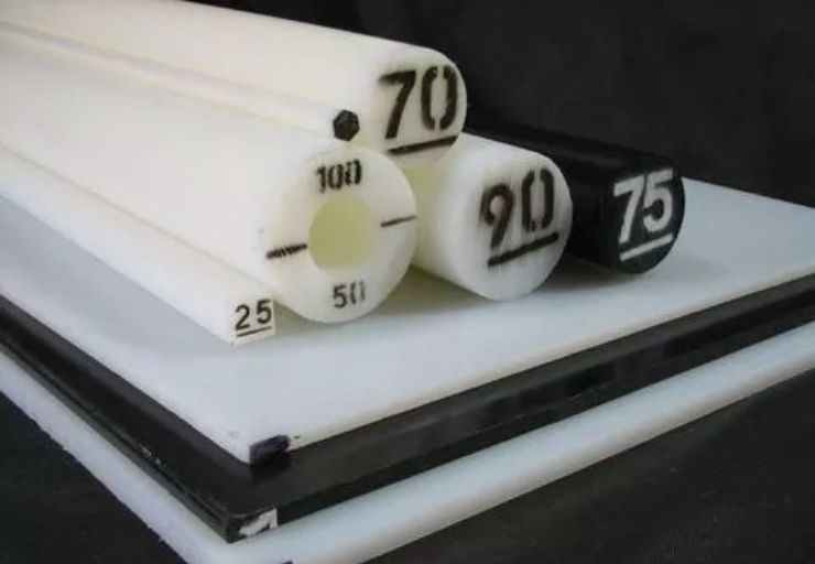 Chapa e barras redondas de Nylon industrial em tom natural e preto, empilhadas sobre superfície escura, com marcações numéricas de diâmetro gravadas nas peças, textura lisa e uniforme, iluminação de estúdio suave, fotografia industrial realista